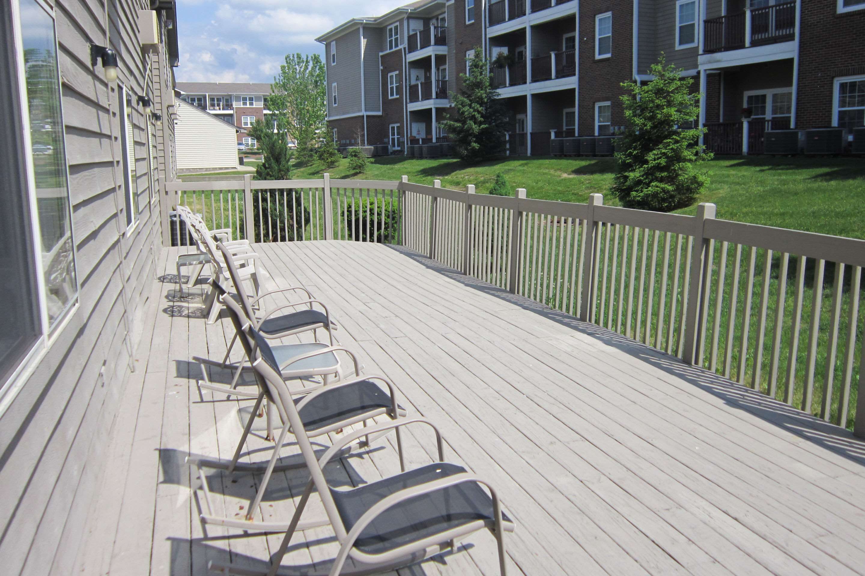 A wooden deck with metal chairs, a railing, and a view of apartment buildings in the background.
