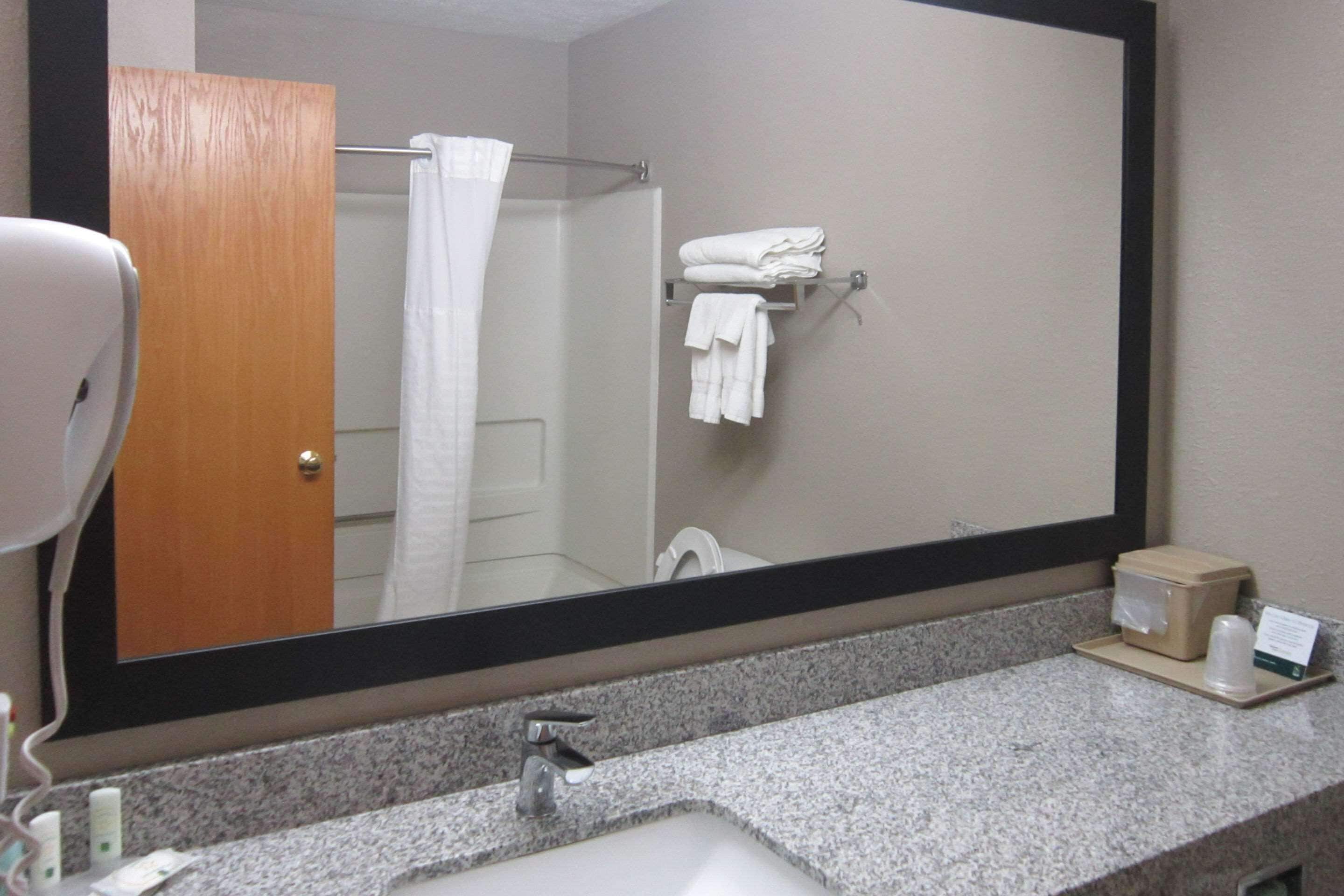 A bathroom with a granite countertop, a sink, a mirror, a towel rack, and a door.