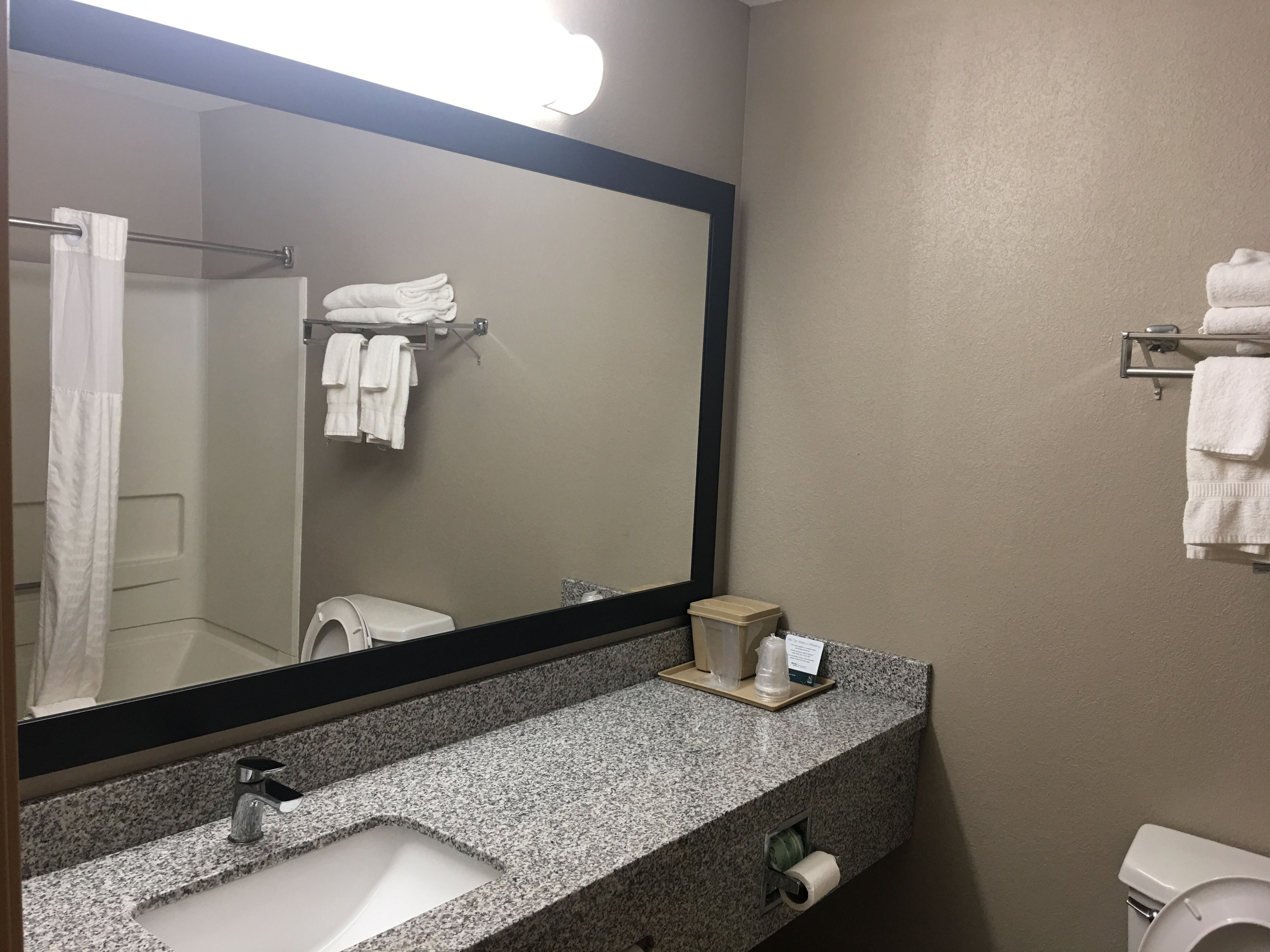 A bathroom with a granite countertop, a sink, a mirror, a towel rack, and a toilet.