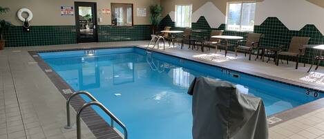 An indoor swimming pool with a lifeguard chair, poolside chairs, and tables.