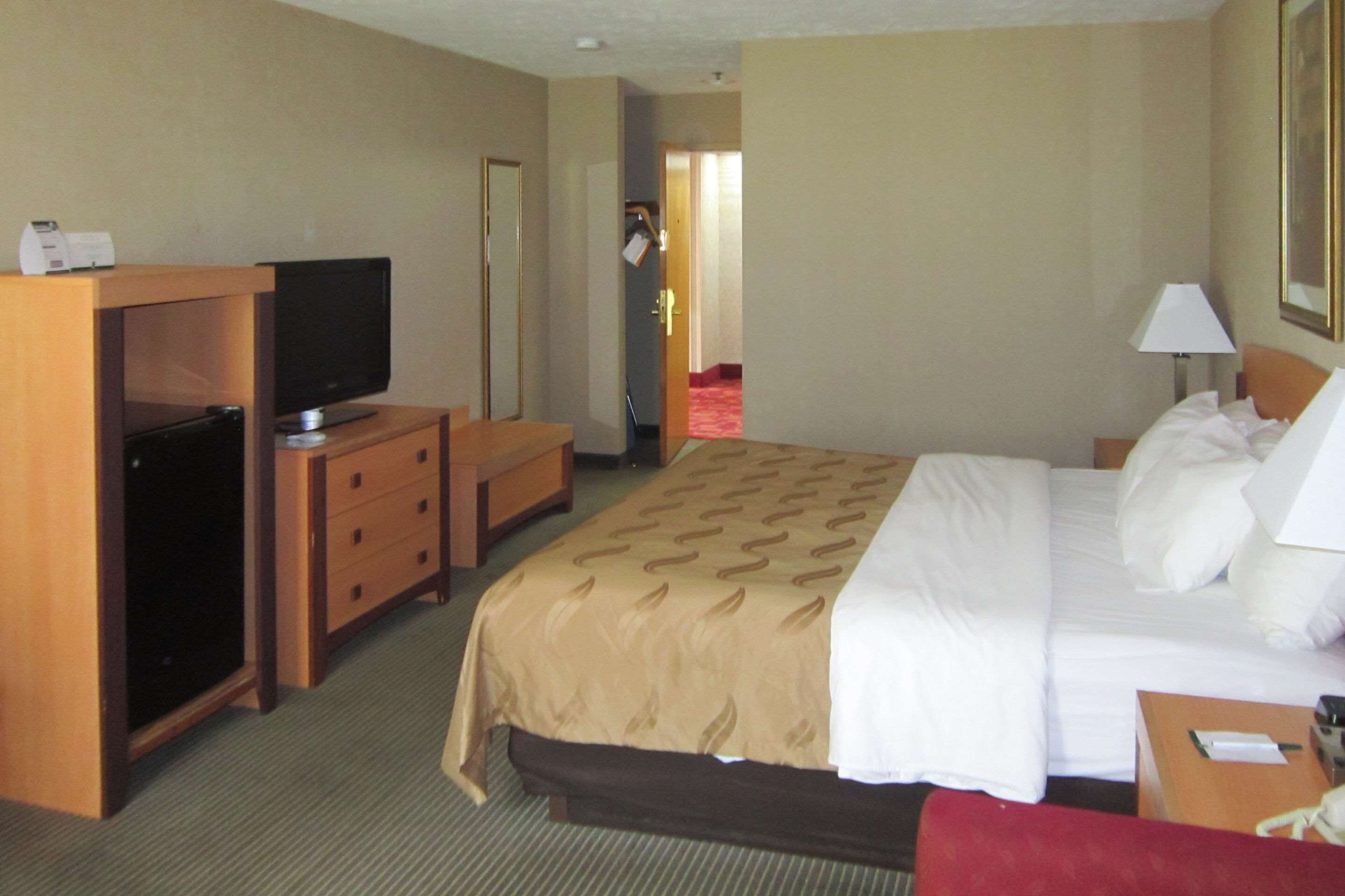 Ein Hotelzimmer mit einem Bett, einem Fernseher auf einem Holzboden, einem Schreibtisch und einer Lampe.