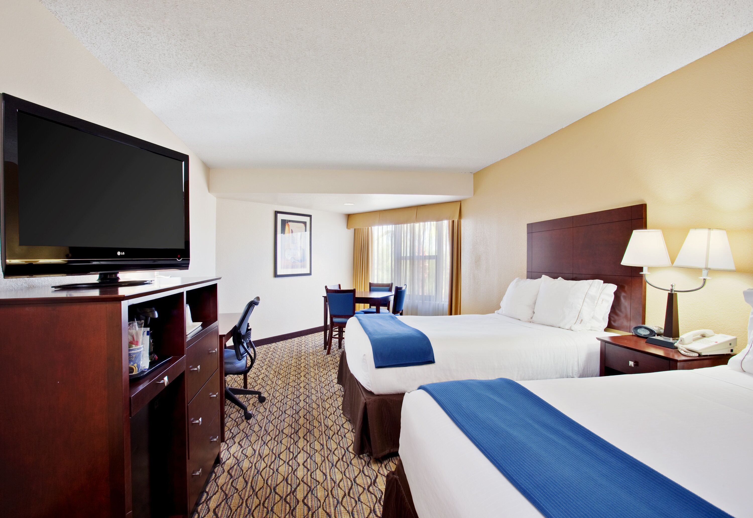 A hotel room with a bed, a desk, a television, and a telephone.