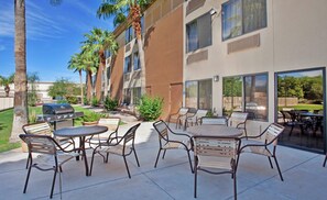 An outdoor patio area with multiple tables and chairs, a barbecue grill, and a view of a building with large windows. - Holiday Inn Express Scottsdale North by IHG (Paradise Valley)