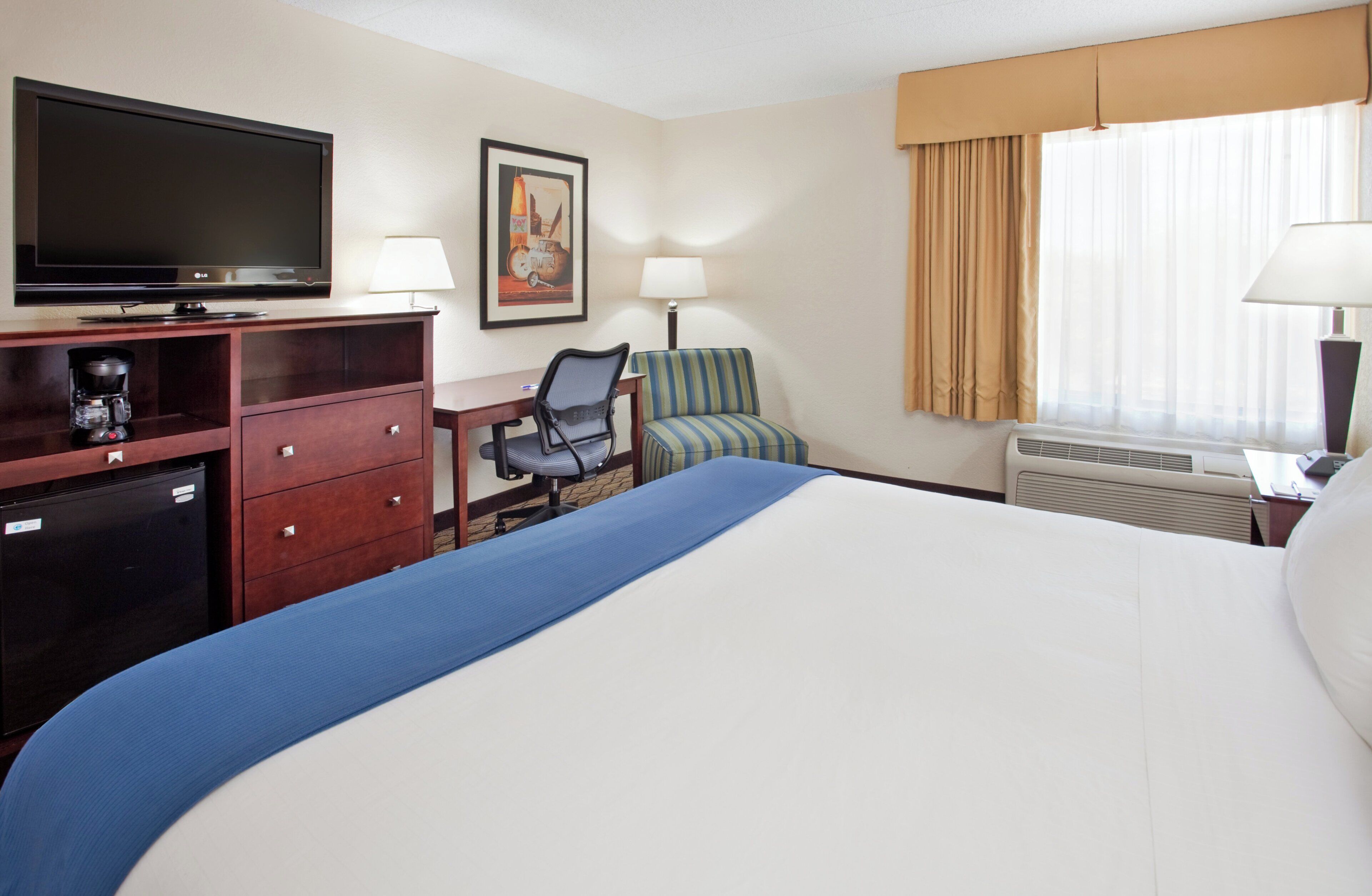 A hotel room with a bed, a desk, a chair, a television, a coffee maker, and a picture on the wall.