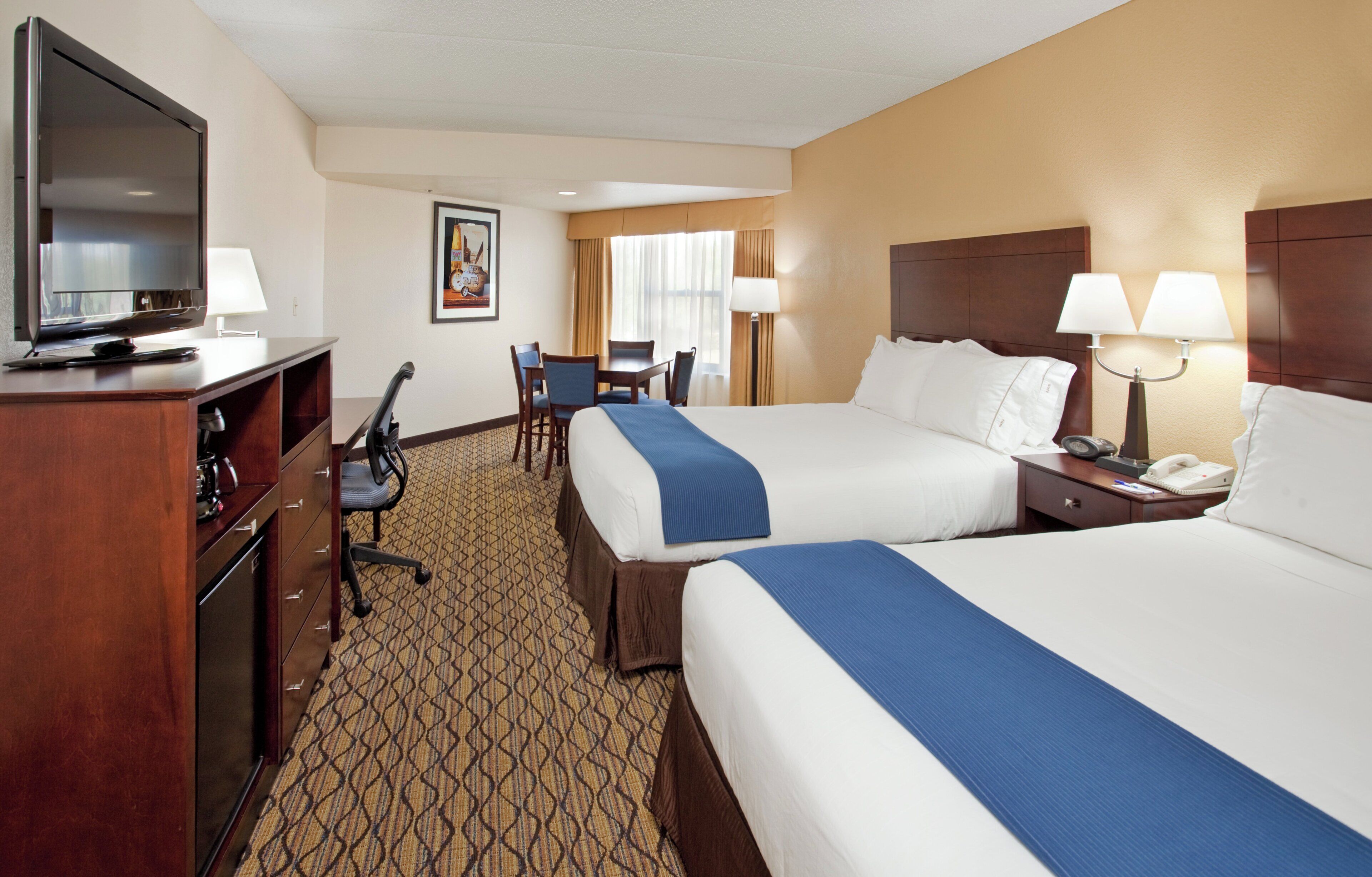 A hotel room with two beds, a desk, a chair, a television, and a telephone.