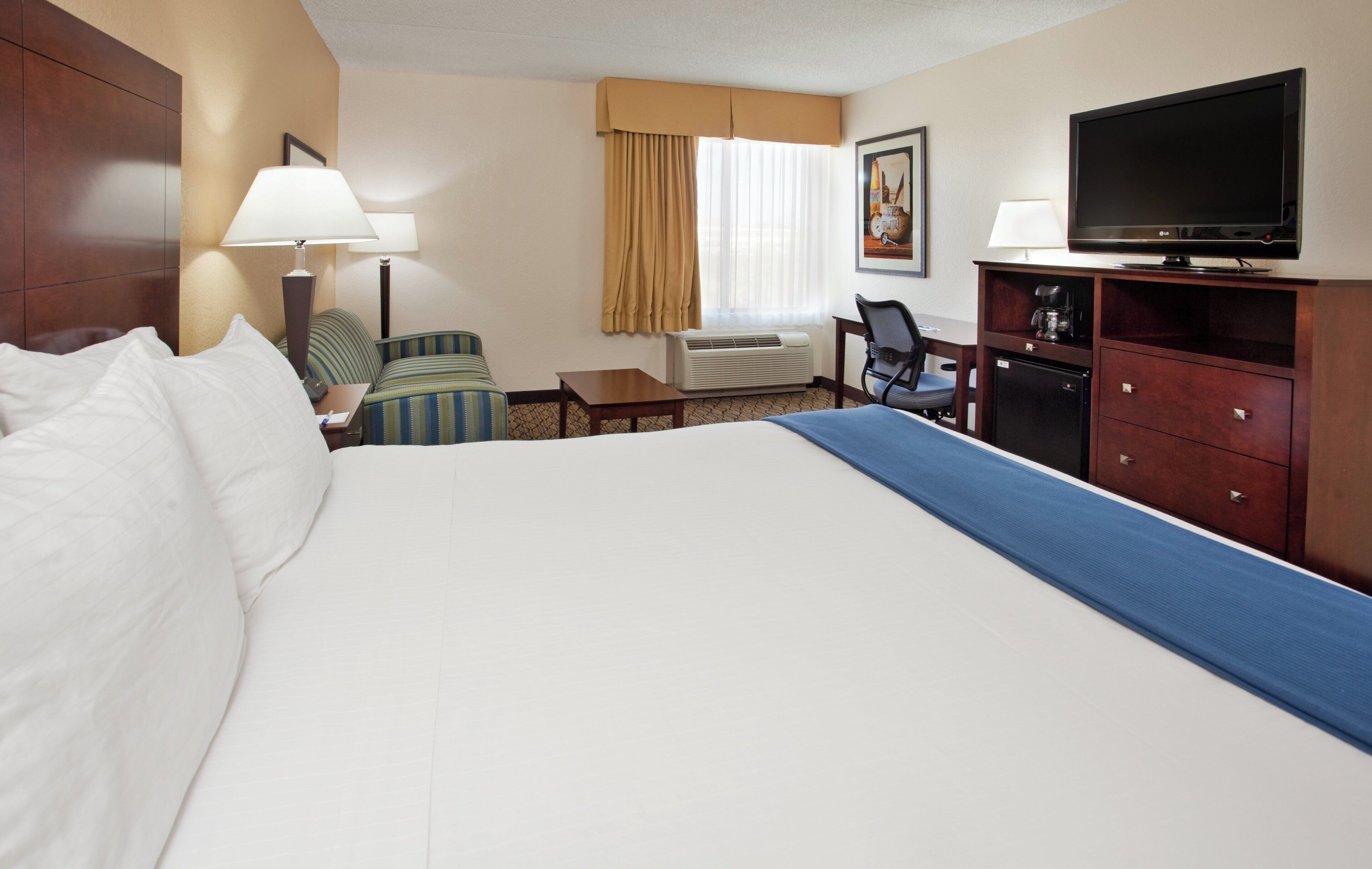 Quarto de hotel com cama grande, escrivaninha, cadeira, televisão e cafeteira.