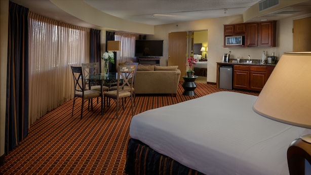 Una habitación de hotel con una cama grande, una mesa de comedor con sillas, un sofá, una televisión y una kitchenette.