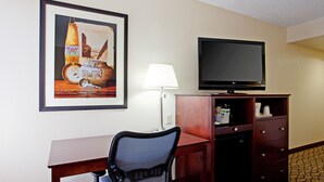 Habitación de hotel con escritorio, silla, televisor, lámpara y un cuadro en la pared.