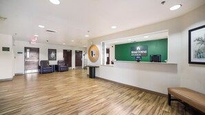 A reception area with a green wall, a reception desk, and a wooden floor. - HomeTowne Studios by Red Roof St. Louis - Airport/ N Lindbergh (Hazelwood)