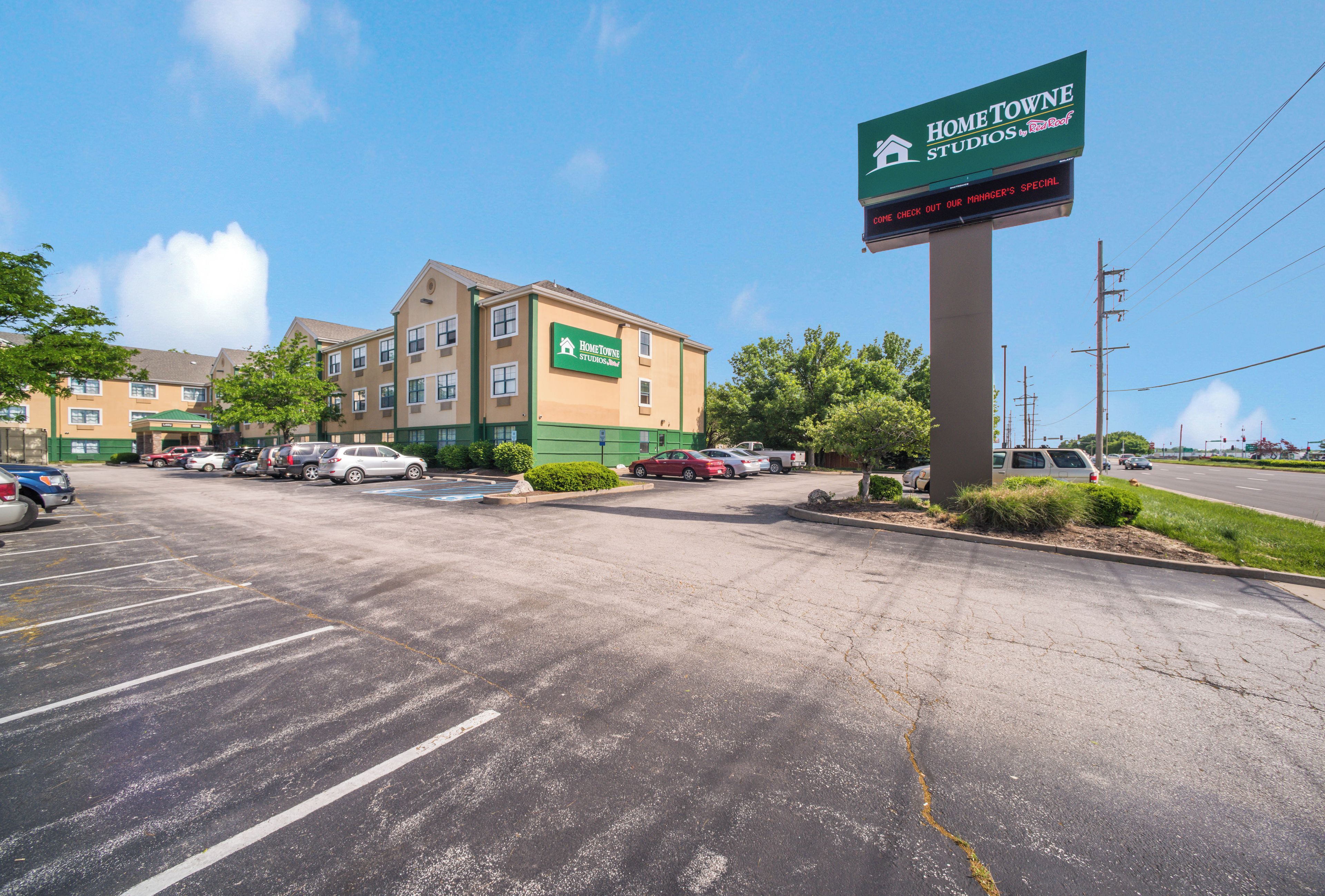 A parking lot with multiple cars, a building with a green and beige facade, and a sign for Home Towne Studios.