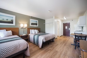 Habitación de hotel con dos camas, un escritorio, una silla, un armario y la puerta del baño.