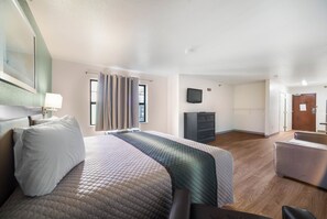 A hotel room with a bed, a desk, a chair, a flat-screen TV, and a wooden floor. - HomeTowne Studios by Red Roof St. Louis - Airport/ N Lindbergh (Hazelwood)