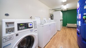 A laundry area with a front-loading washer, a dryer, and a vending machine. - HomeTowne Studios by Red Roof St. Louis - Airport/ N Lindbergh (Hazelwood)