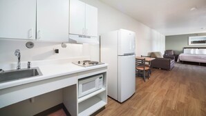 A compact kitchen with a sink, stove, and white cabinets. - HomeTowne Studios by Red Roof St. Louis - Airport/ N Lindbergh (Hazelwood)