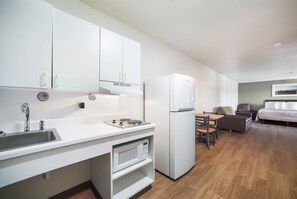 A compact kitchen with a sink, stove, and white cabinets. - HomeTowne Studios by Red Roof St. Louis - Airport/ N Lindbergh (Hazelwood)