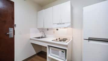 Una kitchenette funcional con un lavamanos, estufa, microondas y refrigerador blanco.