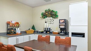 Habitación de hotel con una mesa de comedor, sillas, una estación de café con cafetera, un refrigerador y un adorno en la pared.