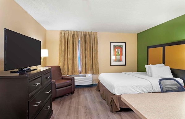 A hotel room with a bed, a desk, a TV, a chair, and a window with curtains.