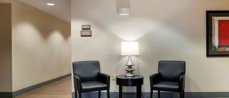 A hotel lobby with two black leather chairs, a table with a lamp, and an exit sign above.