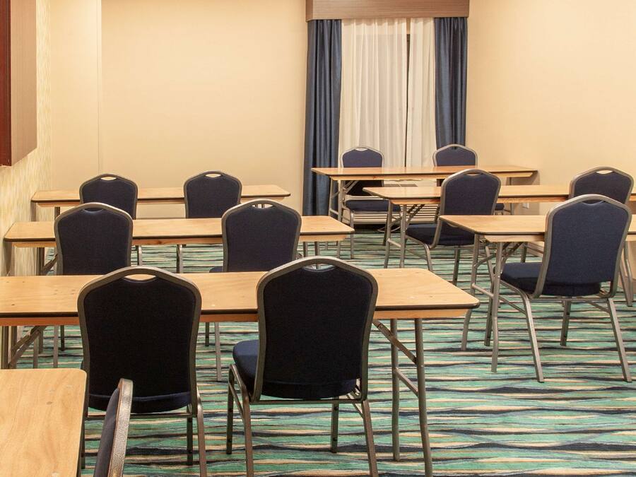 A conference room with multiple tables and chairs, carpeted floor, and a window with curtains.