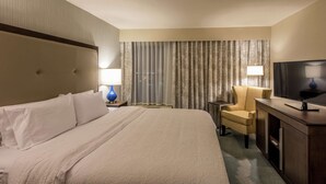 A hotel room with a large bed, a desk with a television, a chair, and a window with curtains. - Hampton Inn & Suites Jackson-Coliseum (Jackson)