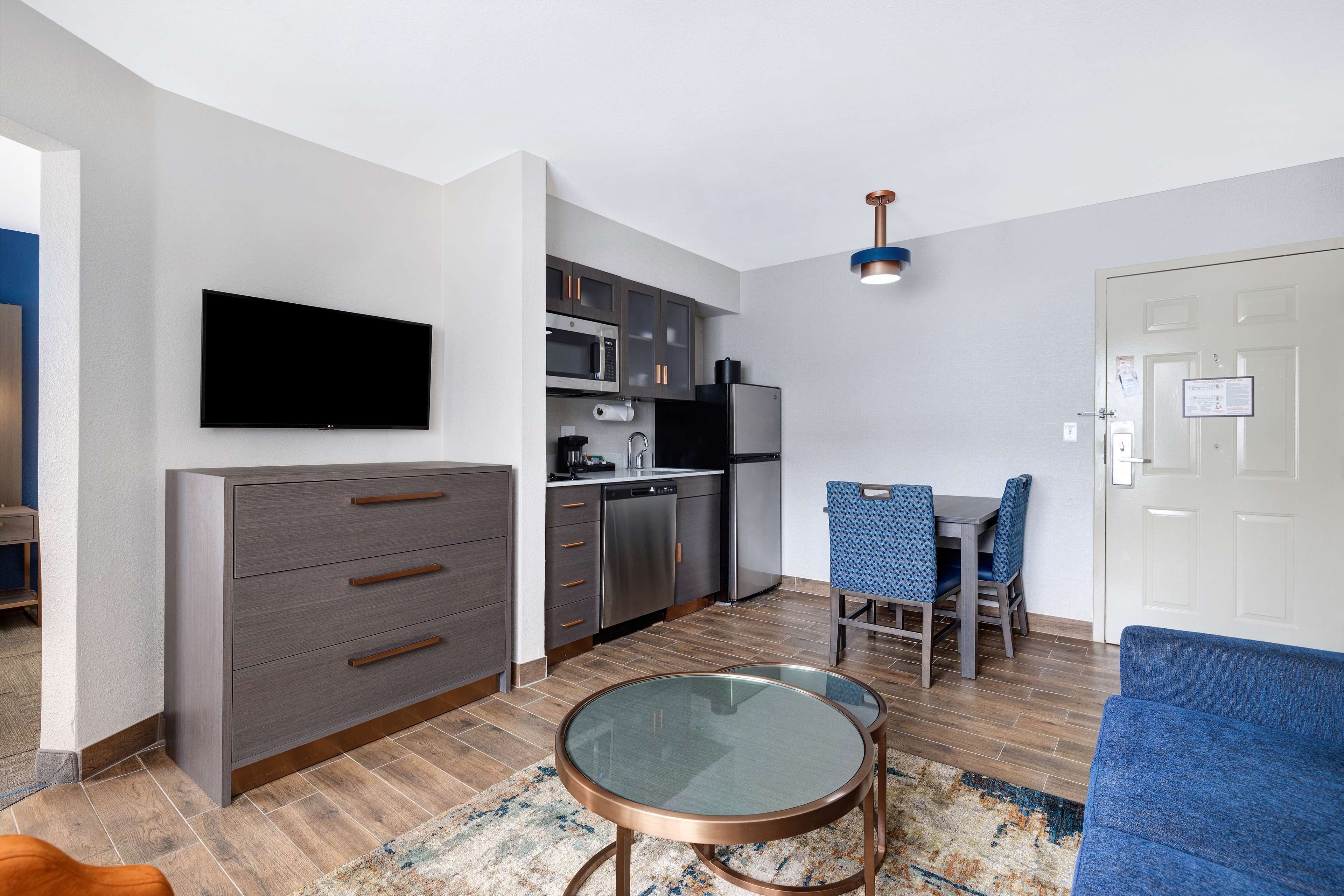 Ein modernes Wohnzimmer mit Flachbildfernseher, einem grauen Schrank, einem Glastisch und einem blauen Sofa.