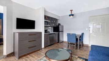 Ein modernes Wohnzimmer mit Flachbildfernseher, einem grauen Schrank, einem Glastisch und einem blauen Sofa.