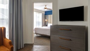 Quarto de hotel com cama, televisão fixada na parede, chão de madeira e uma cadeira.