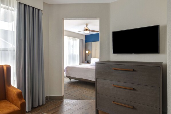 A hotel room with a bed, a TV mounted on the wall, a wooden floor, and a chair. - Homewood Suites by Hilton Jackson-Ridgeland (Ridgeland)