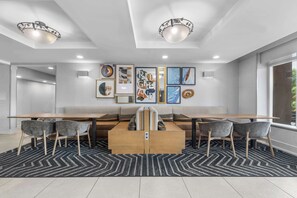 A modern dining area with a long table, cushioned seating, and a patterned rug.