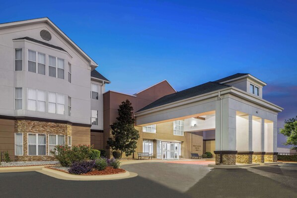 A modern hotel with a central entrance, a stone facade, and a well-maintained garden area.