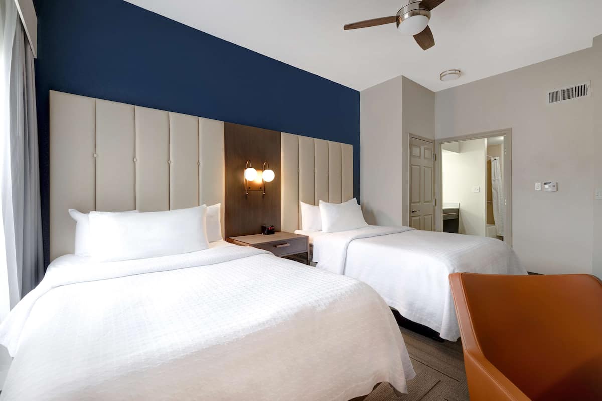 A hotel room with two beds, a nightstand, a chair, and a ceiling fan.