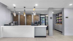 Uma área de recepção de hotel com um balcão branco, um minibar e uma máquina de bebidas para autoatendimento.