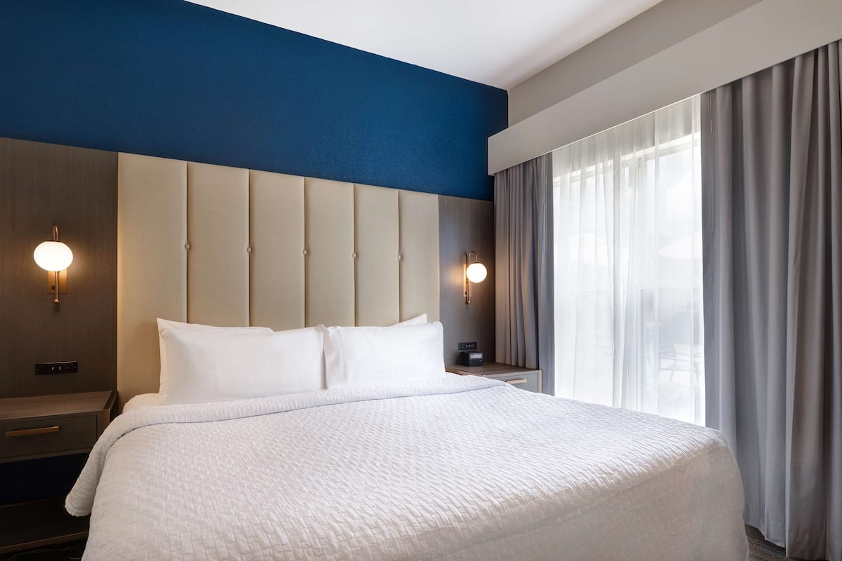 A hotel room with a large bed, two bedside tables, a wall-mounted light, and a window with curtains.