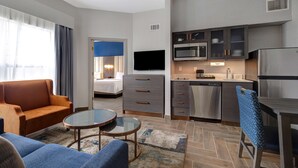 Quarto de hotel moderno com área de estar, cozinha compacta e uma cama.