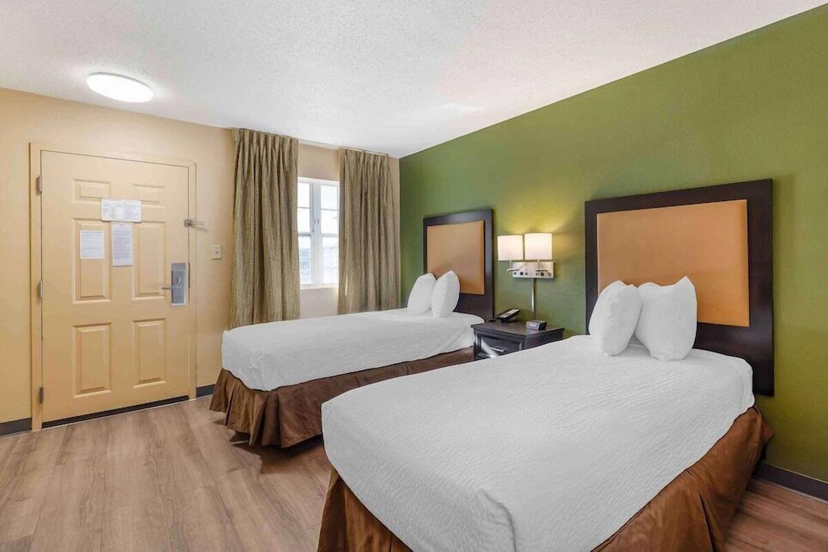 A hotel room with two beds, a door with a notice, a window with curtains, and a green wall.