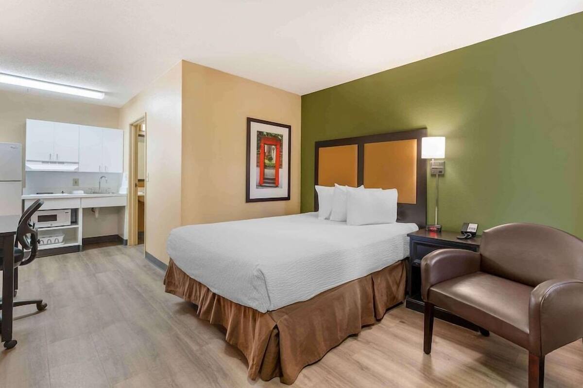 A hotel room with a bed, a desk, a chair, and a kitchenette.