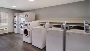 A laundry room with multiple washing machines and dryers, a ventilation system, and a window with blinds. - MainStay Suites Omaha Old Mill (Omaha)
