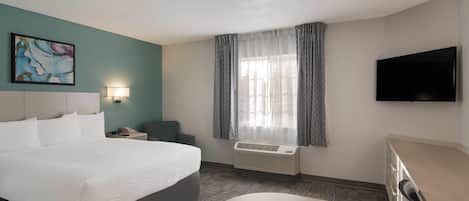 Une chambre d’hôtel avec un grand lit, un bureau, une chaise, un téléviseur à écran plat, une fenêtre avec des rideaux et un appareil de climatisation.