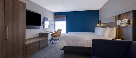 A hotel room with a bed, a desk with a chair, a TV, and a large wardrobe.