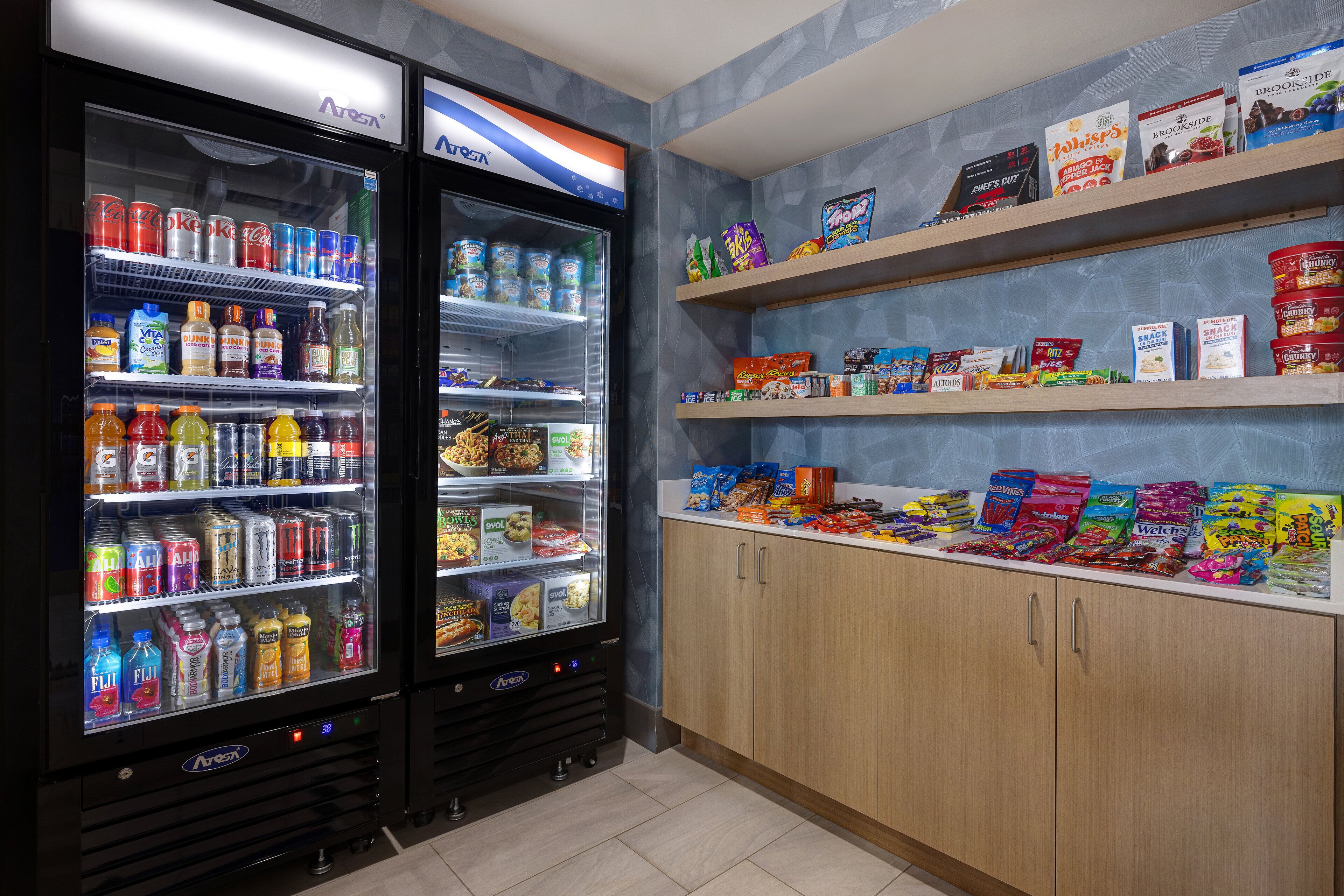 A vending area with two refrigerated beverage dispensers and shelves stocked with snacks and beverages.