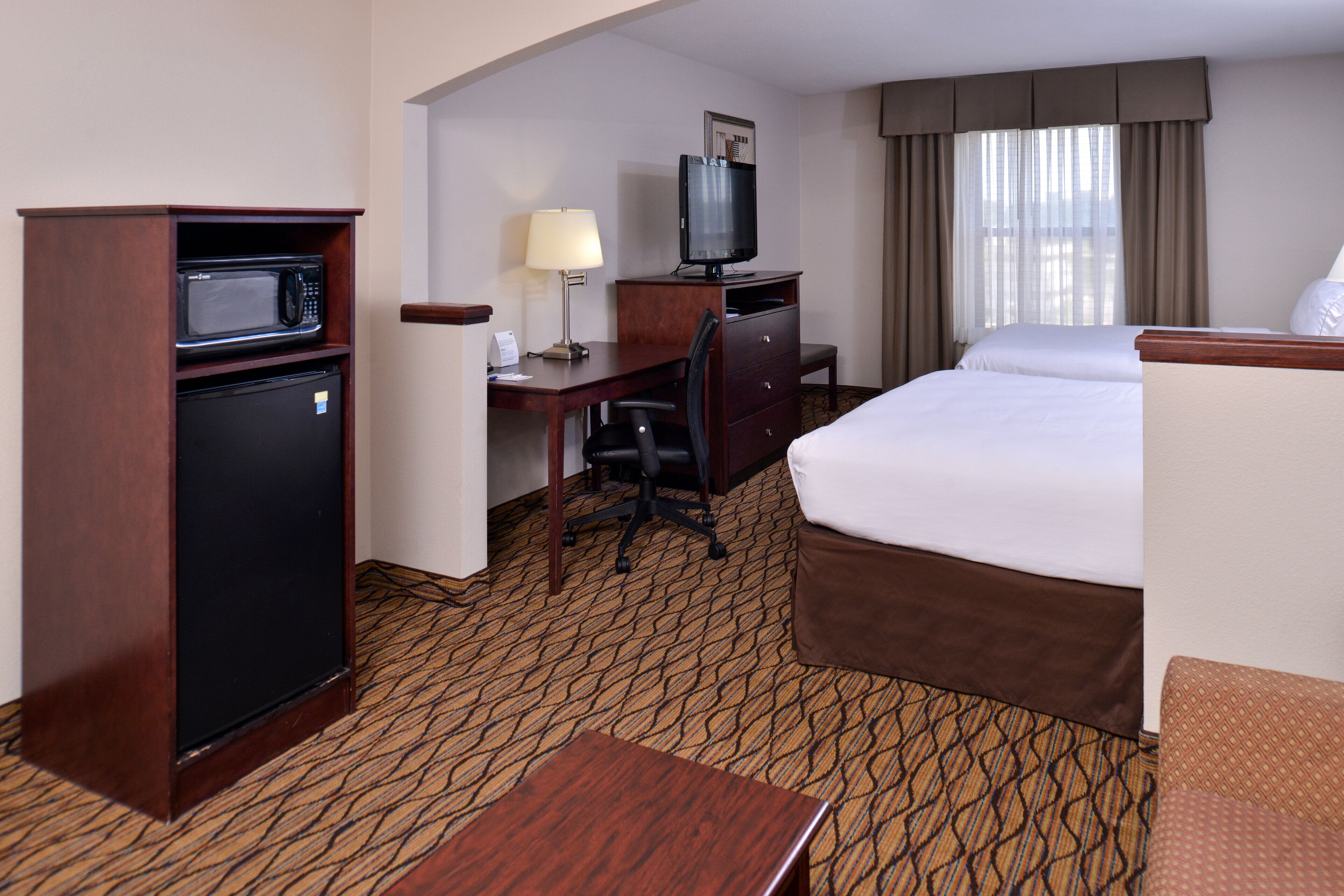 Una habitación de hotel con cama, escritorio, computadora, microondas y televisor.