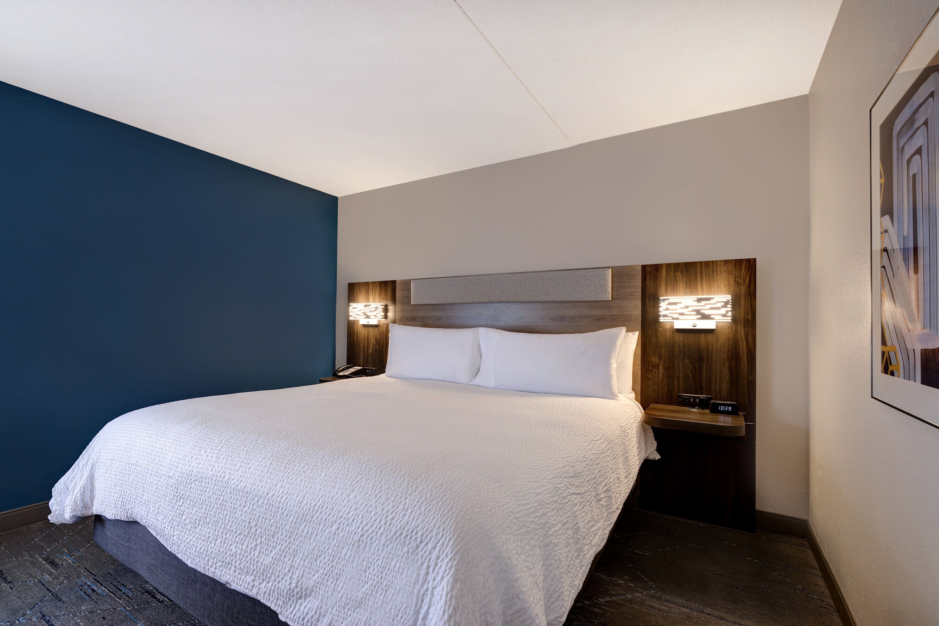 Una habitación de hotel con una cama grande, dos mesitas de noche e iluminación en la pared.