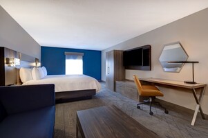 Une chambre d’hôtel moderne équipée d’un lit, d’un bureau, d’une chaise, d’une télévision et d’un grand miroir.