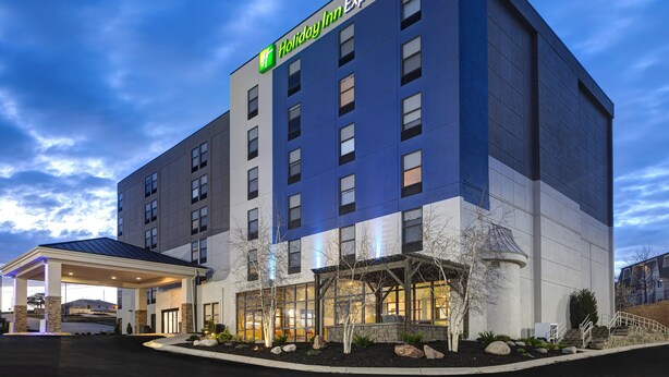 A Holiday Inn Express hotel with a modern design, featuring a covered entrance and a landscaped area with trees and rocks. - Holiday Inn Express & Suites Central Omaha by IHG (Omaha)