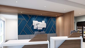 A modern hotel reception area with two reception desks, a blue geometric wall design, and a wooden panel accent. - Holiday Inn Express & Suites Central Omaha by IHG (Omaha)