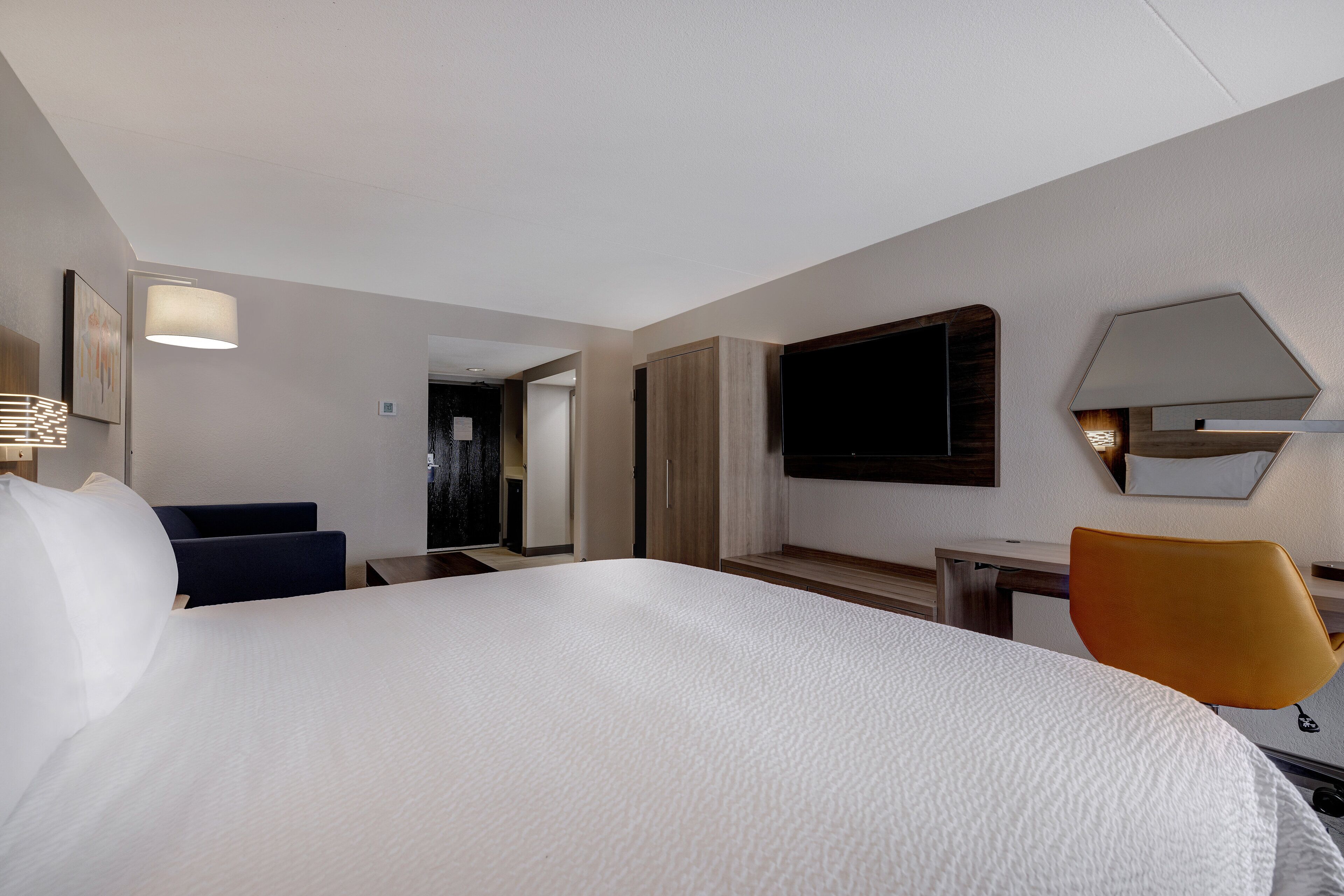 A hotel room with a large bed, a desk, a chair, a TV, and a mirror on the wall.