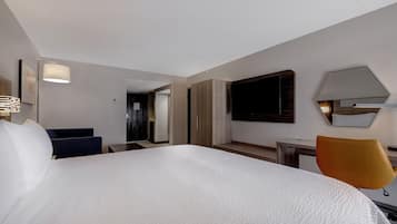 A hotel room with a large bed, a desk, a chair, a TV, and a mirror on the wall.