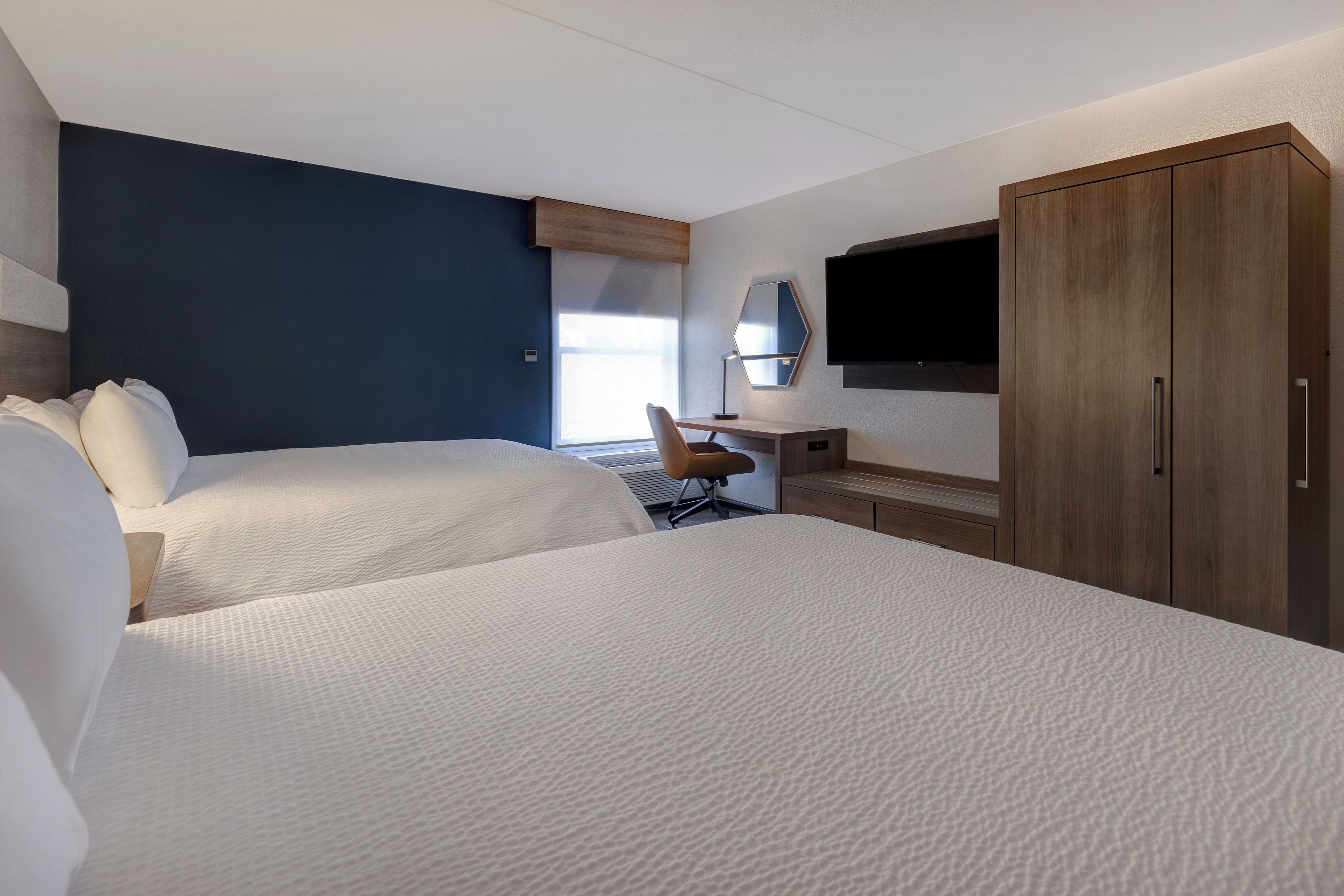 Ein Hotelzimmer mit zwei Betten, einem Schreibtisch, einem Sessel, einem Fernseher und einem Kleiderschrank.