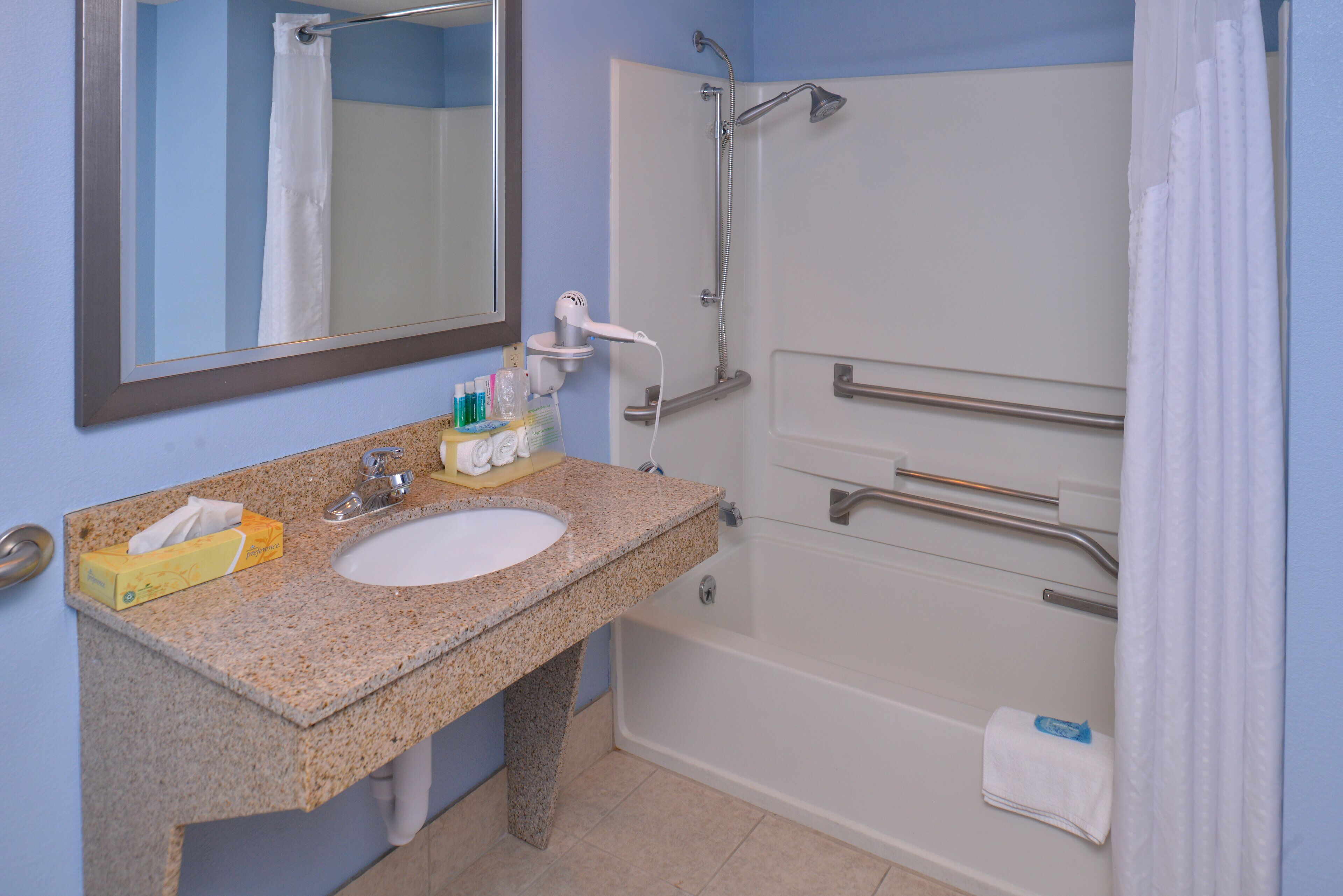 Une salle de bain équipée d’un lavabo en granit, d’un miroir, d’une douche avec des barres d’appui et d’un porte-serviettes.